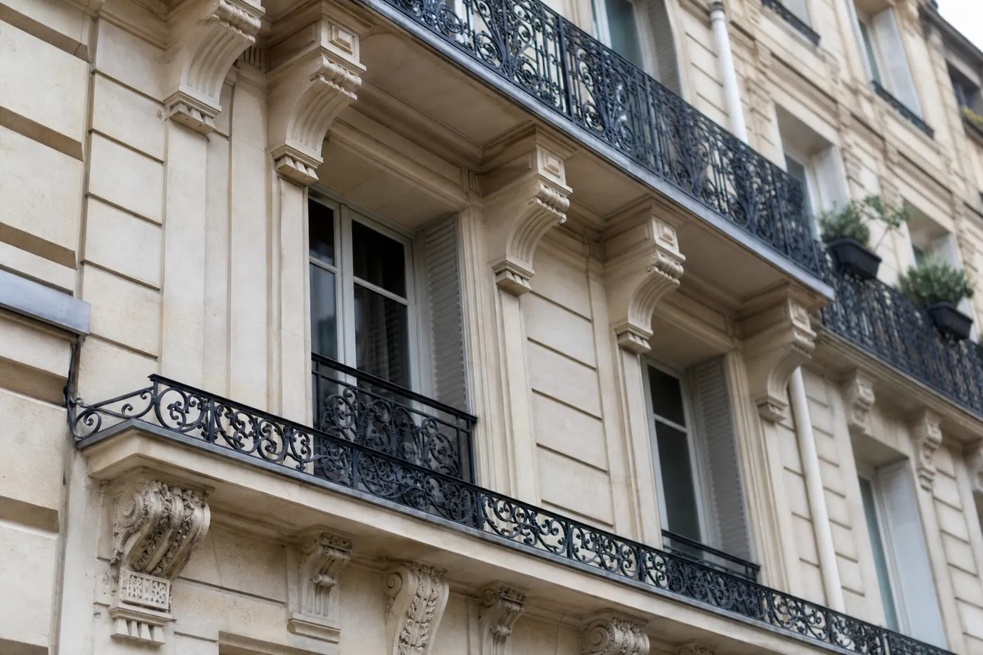 Façade d’immeuble parisien en pierre de taille du XIXᵉ siècle, balcons filants en fer forgé et fenêtres à petits carreaux