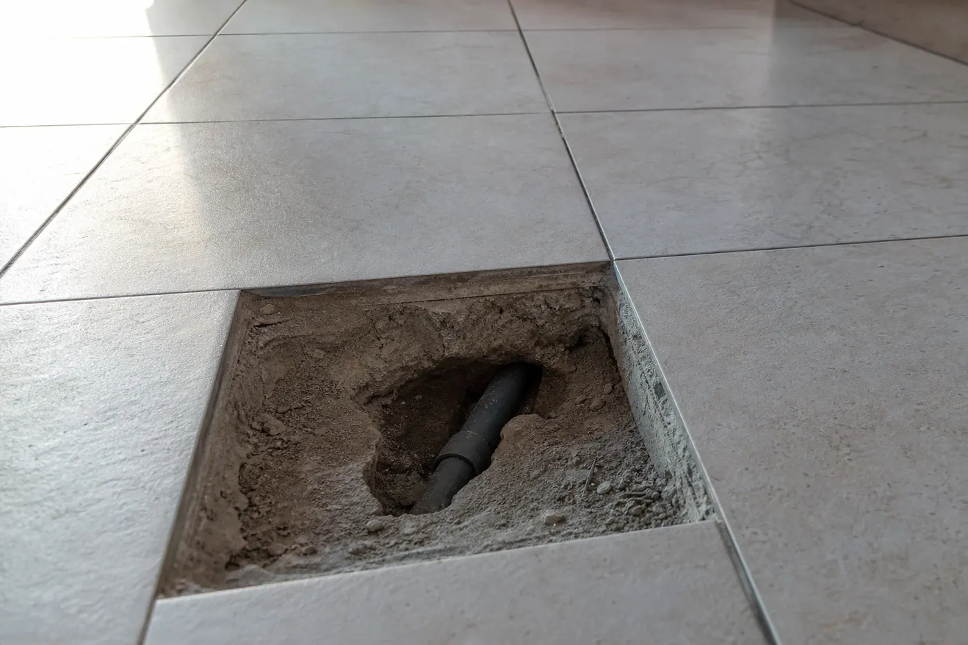 Un seul carreau retiré dans un sol carrelé, ouverture nette dans la chape et canalisation visible, carrelage intact tout autour
