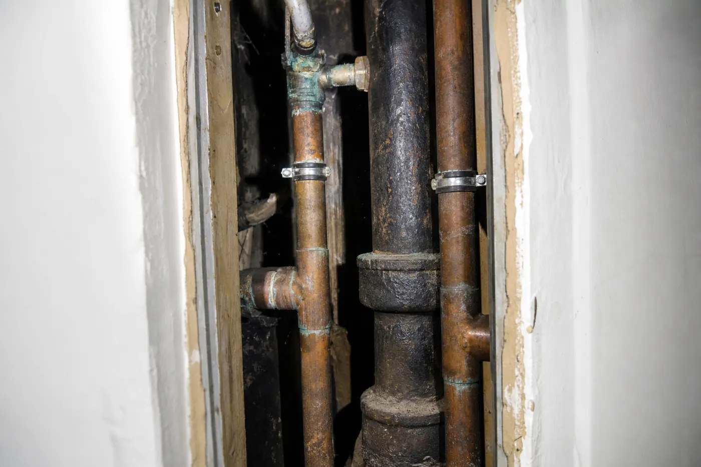 Gaine technique ouverte dans un immeuble ancien, colonne montante verticale en fonte et cuivre oxydé avec ses piquages