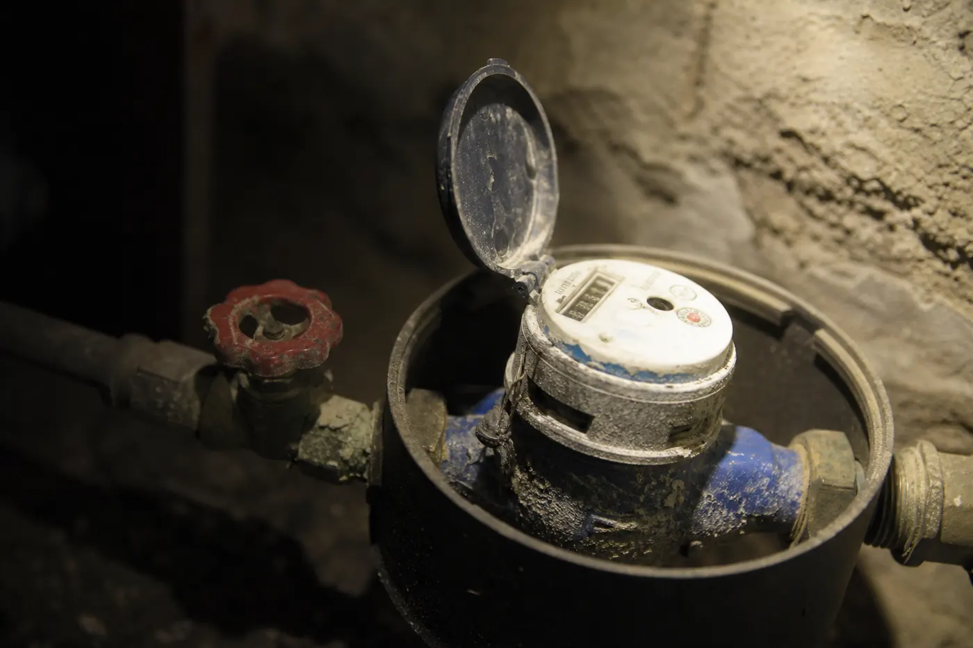 Regard de compteur d’eau ouvert dans une cave d’immeuble, compteur mécanique et vanne d’arrêt entartrés
